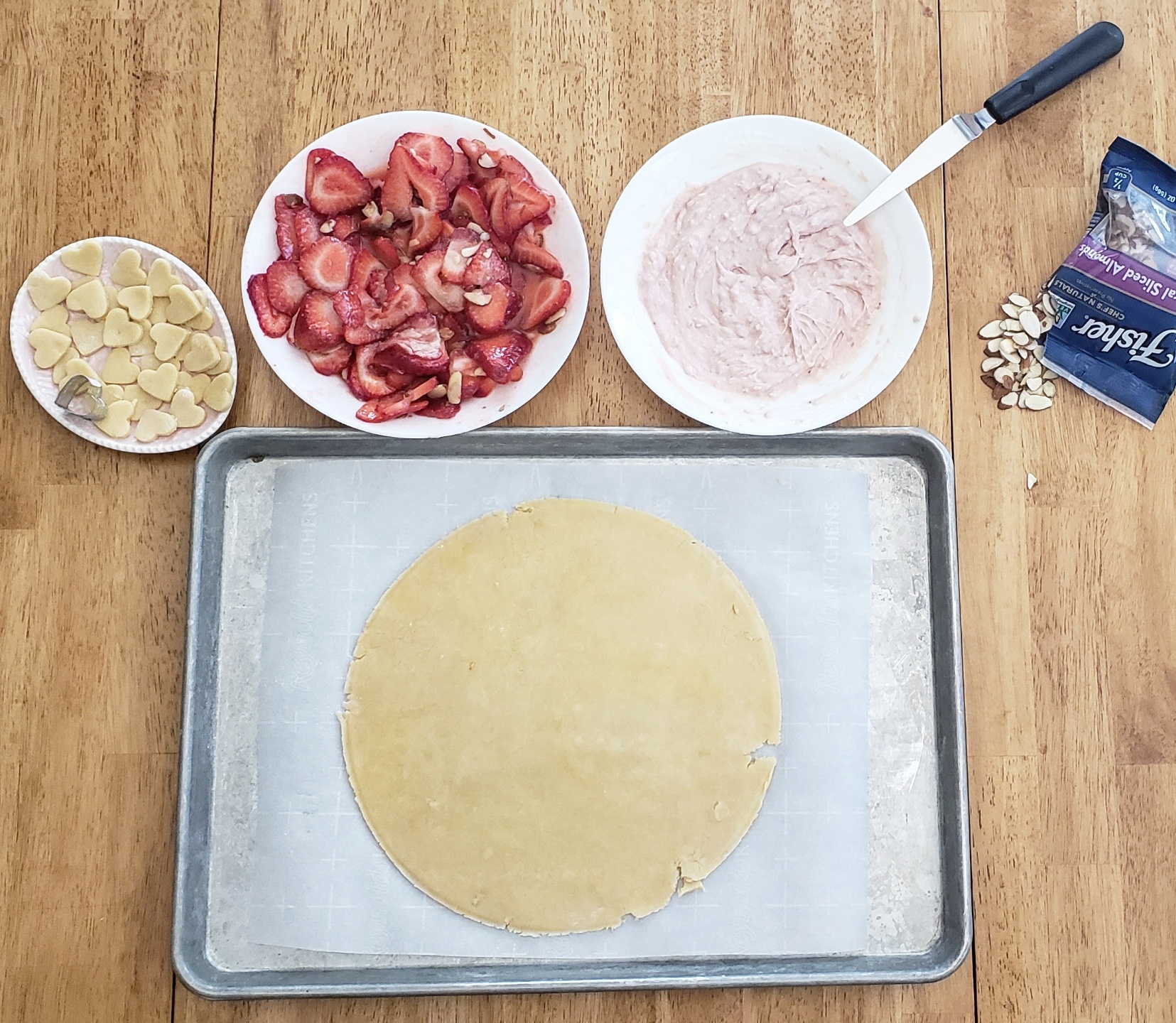 Strawberry crust lying on a baking sheet. 3 plates, one with Pie filling, one with strawberries, and one with dough decorations